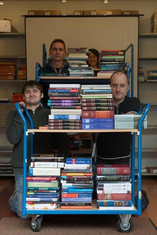 Drei Kolleg:innen von Missing Link mit einem voll beladenen Bücherwagen